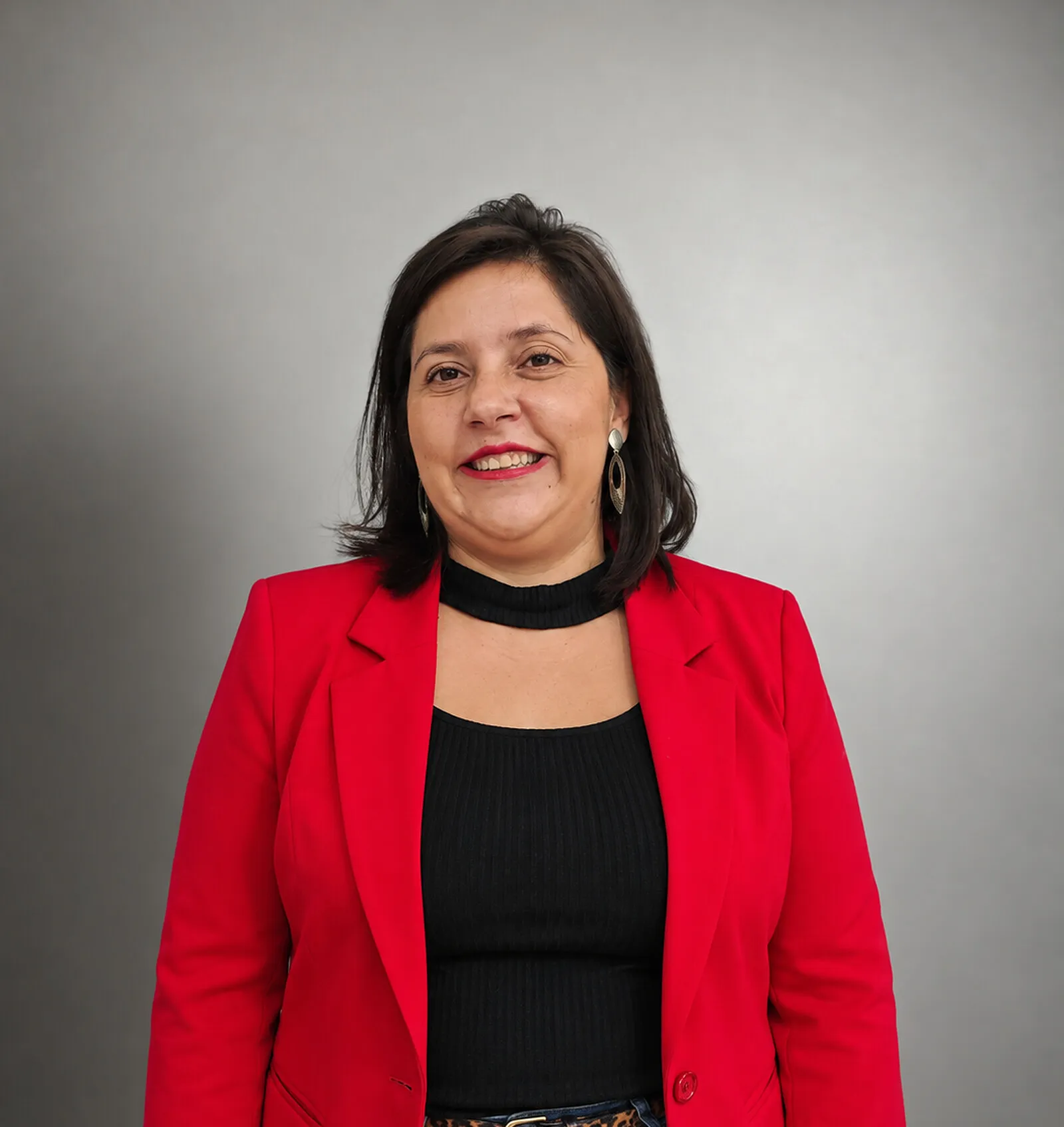 Retrato de Jaqueline Cerezoli, de blazer vermelho, sobre fundo cinza.